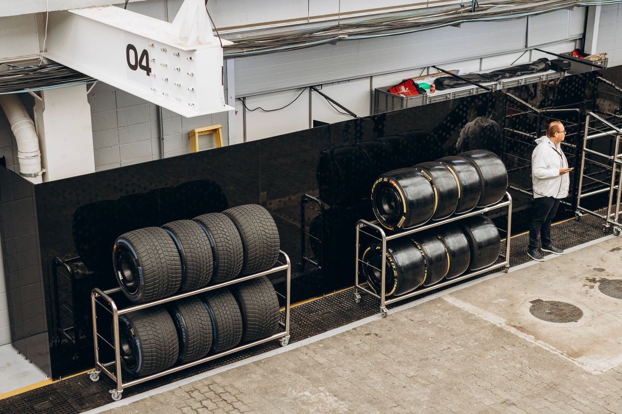 our-story-02 High-performance racing tires stacked in a pit garage with a technician onsite.